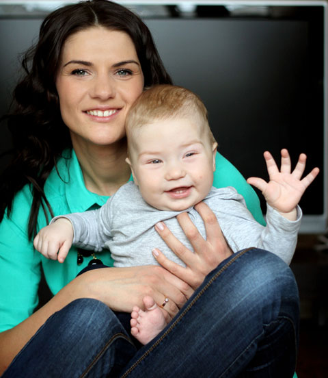 Au-pair mit freundlich winkendem Kleinkind auf dem Schoß